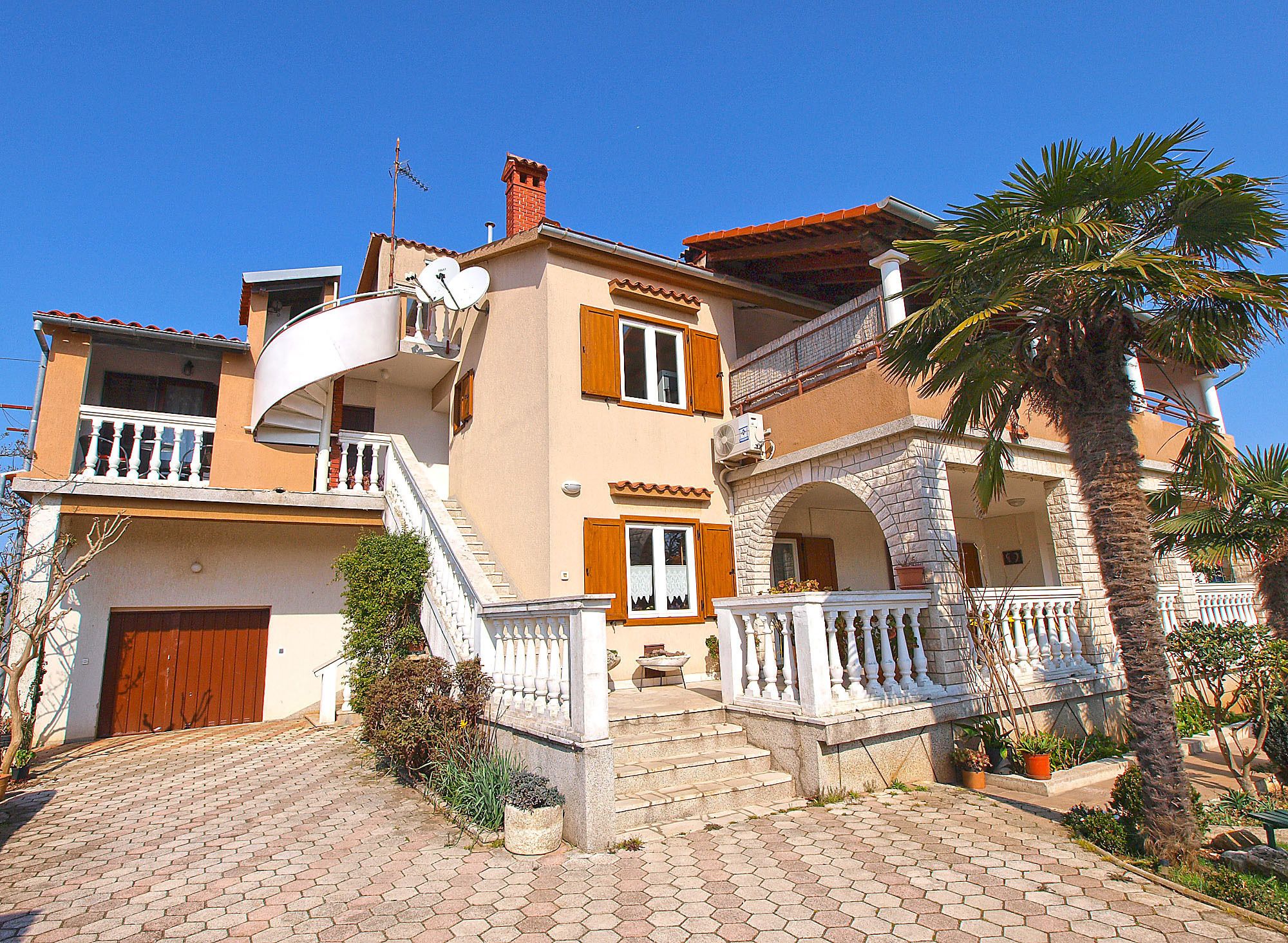 A two-story building with a balcony, a staircase, and a palm tree.