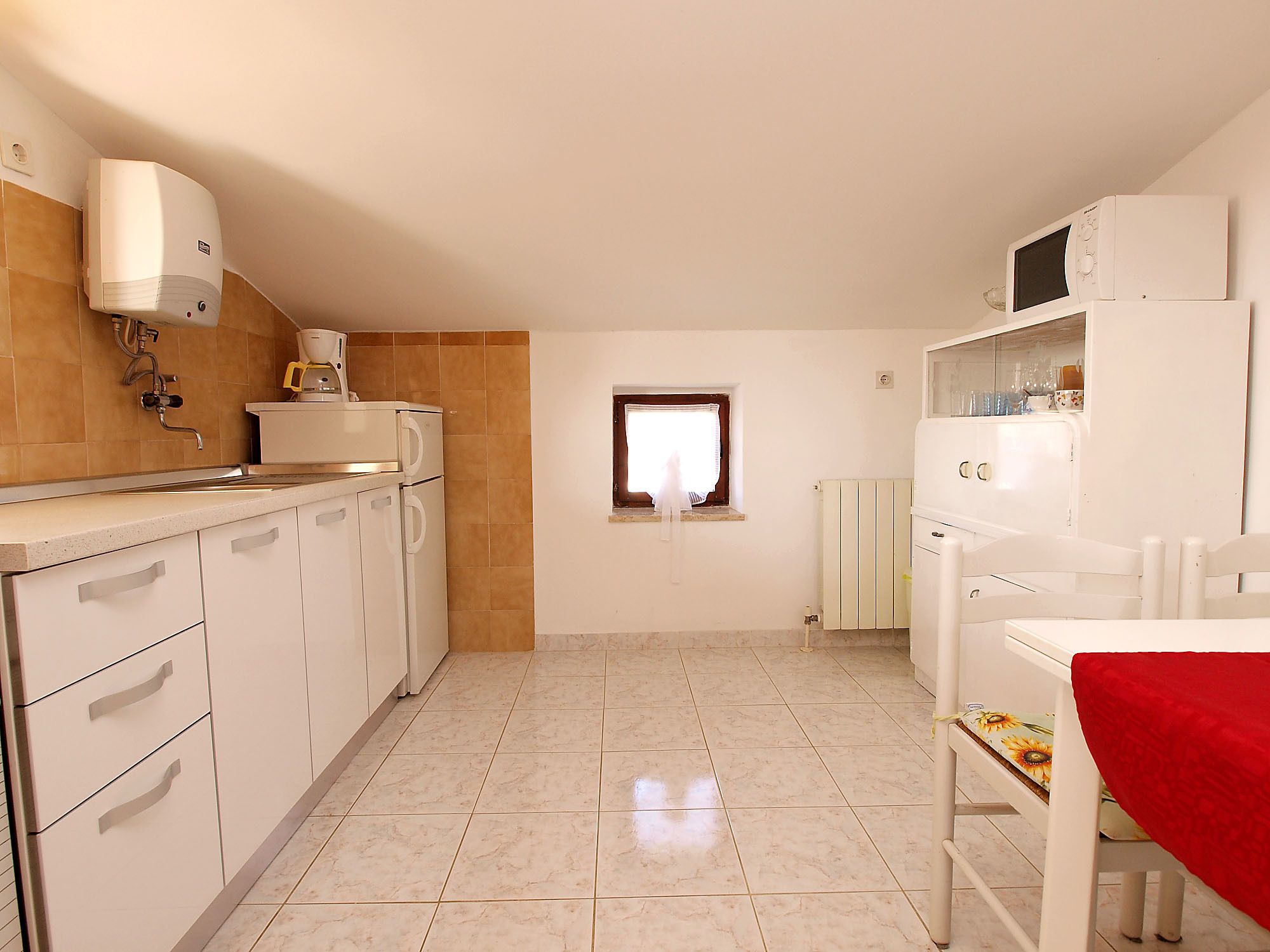 A compact kitchen with a sink, stove, and microwave. There is a window with a view of the outside.