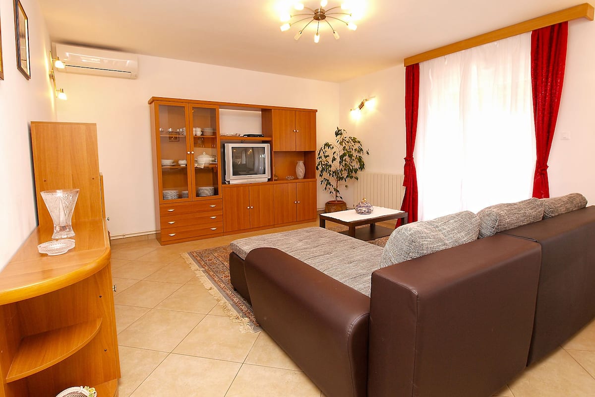 A living room with a sofa, a television, wooden cabinets, and a plant.
