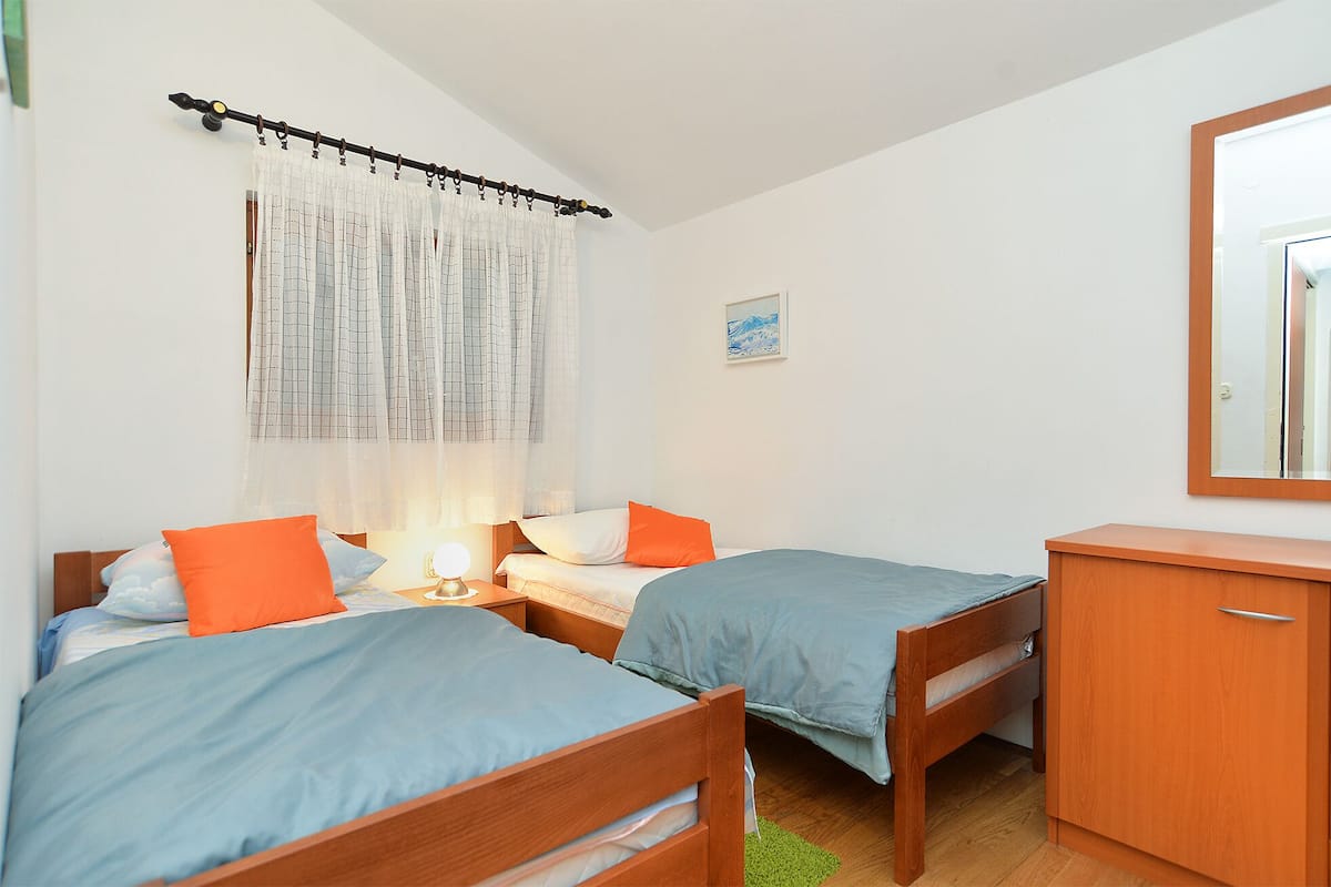 A bedroom with two single beds, a nightstand with a lamp, a wooden dresser, and a window with curtains.