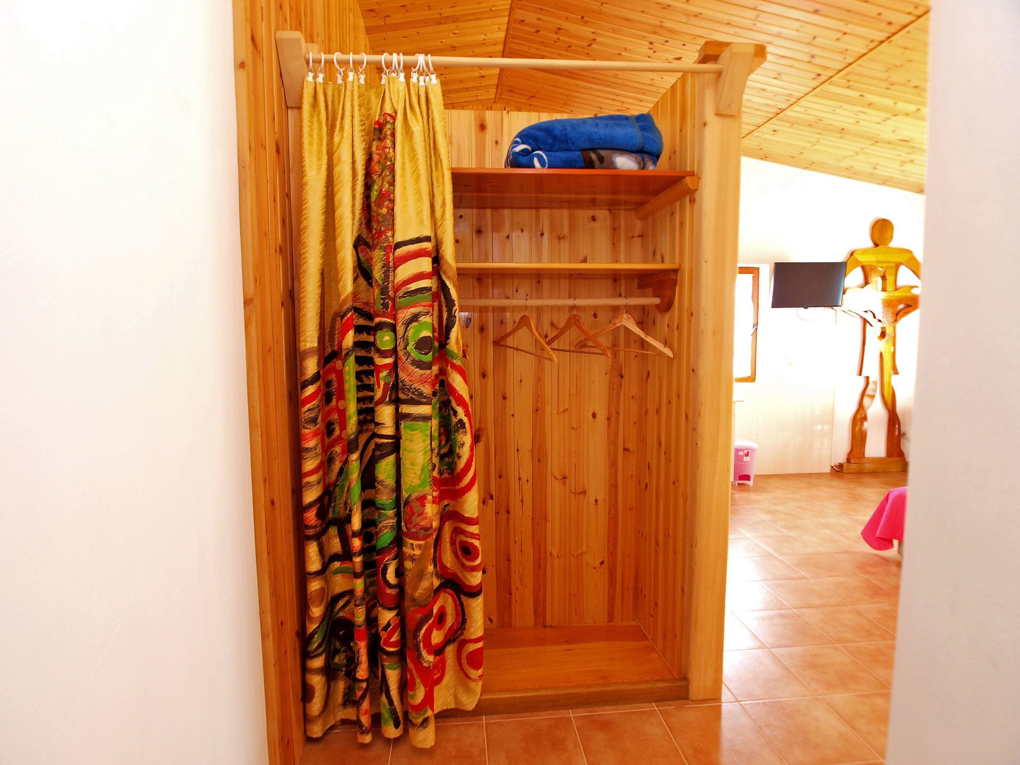 A wooden room with a shower curtain, wooden walls, a shelf with towels, and a wooden figure.