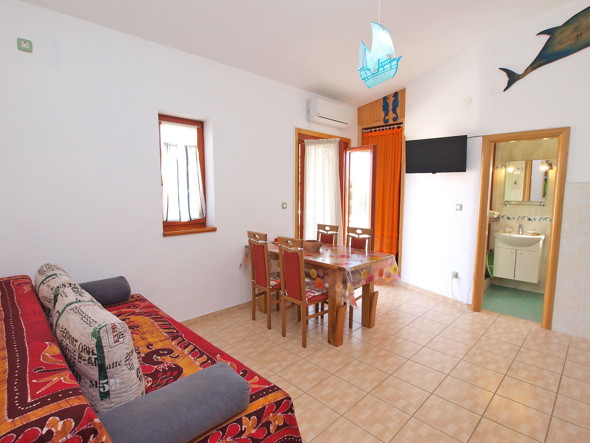 A dining area with a table and chairs, a sofa with a patterned cover, a window, and an air conditioning unit.