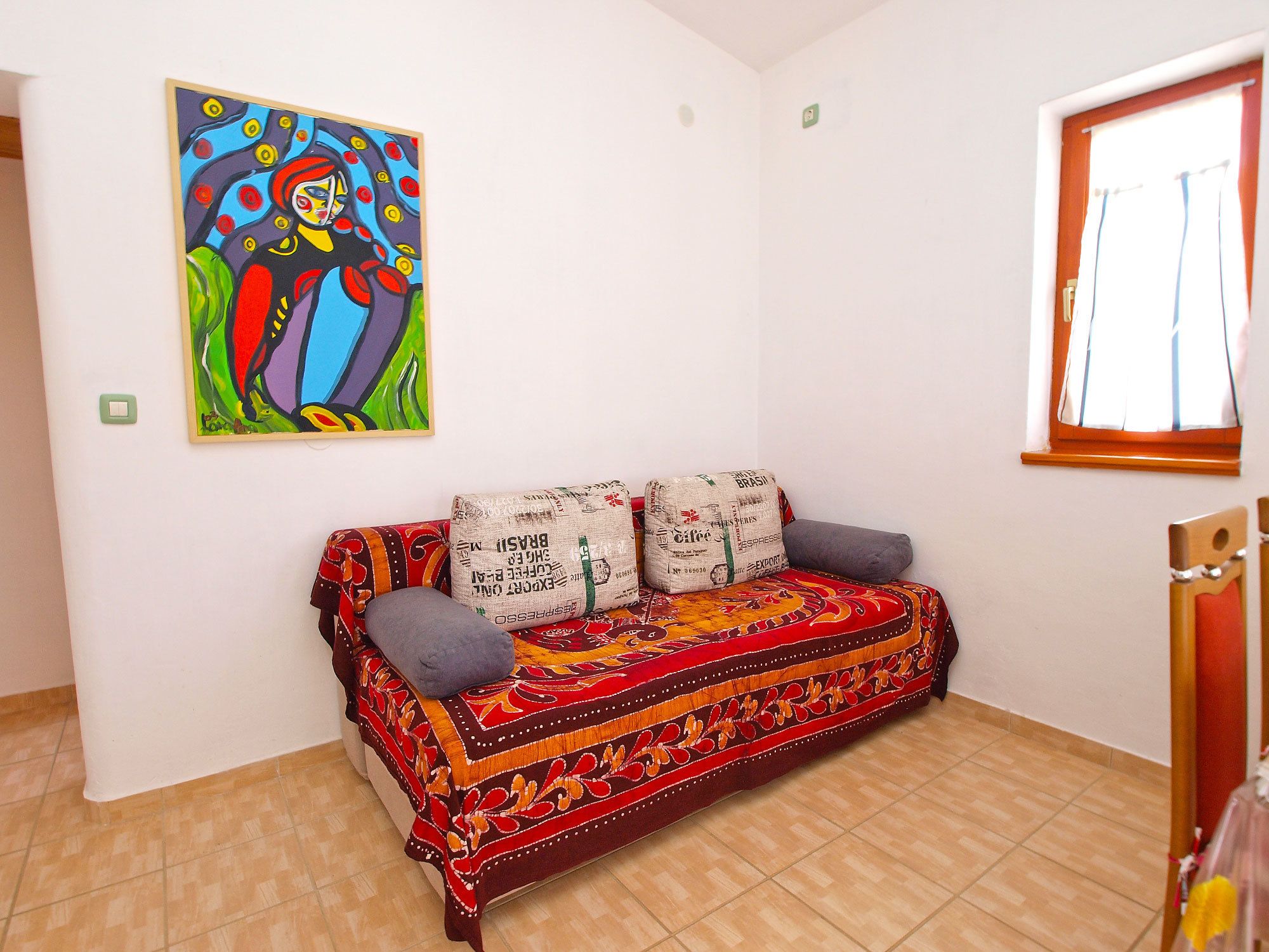 Una habitación con un sofá colorido, un cuadro llamativo y una ventana con cortinas.
