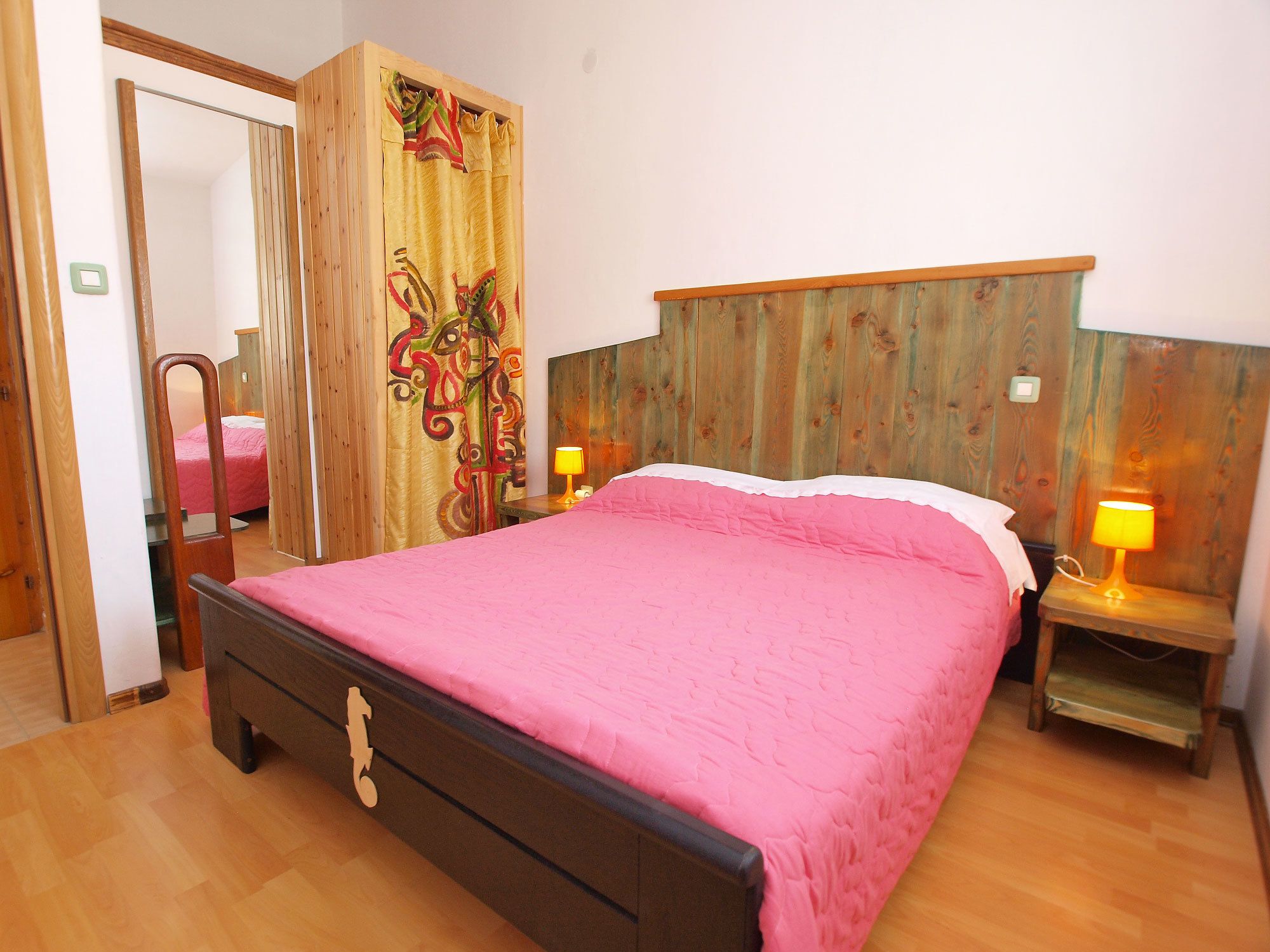 Ein Schlafzimmer mit einem Holz-Kopfteil, einem Bett mit rosa Bettwäsche, zwei Nachttischlampen und einem Holzschrank.