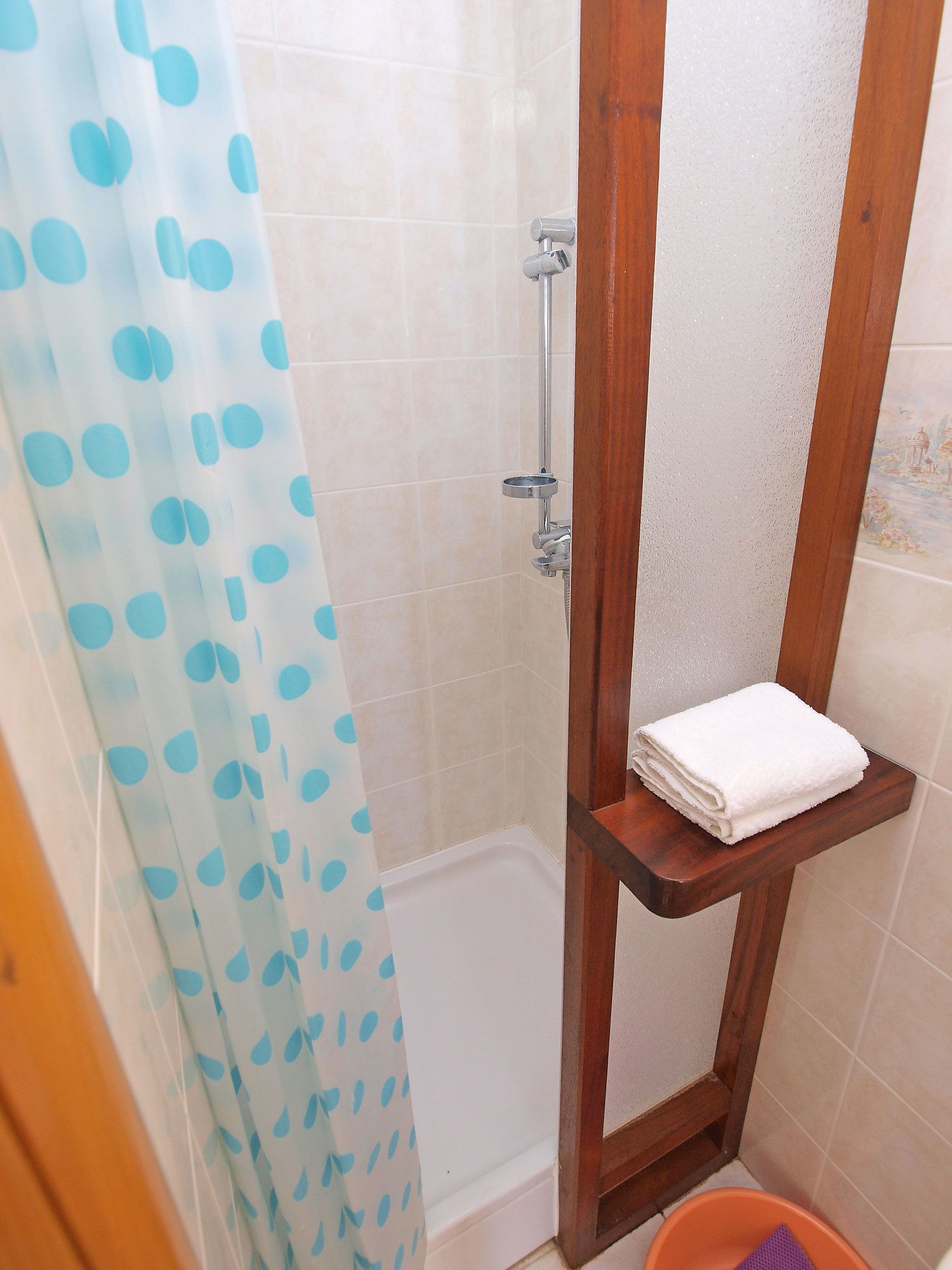 Un angolo doccia con tenda blu a pois, uno scaffale di legno con un asciugamano bianco e un soffione.