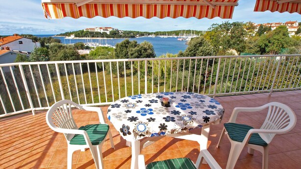 Un balcón con una mesa redonda y cuatro sillas, con vistas a un puerto deportivo y una ciudad costera.
