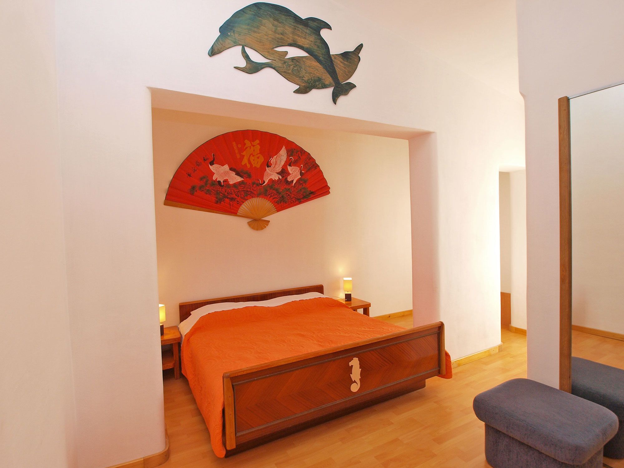 A bedroom with a wooden bed, a red decorative fan, and a dolphin wall art piece.