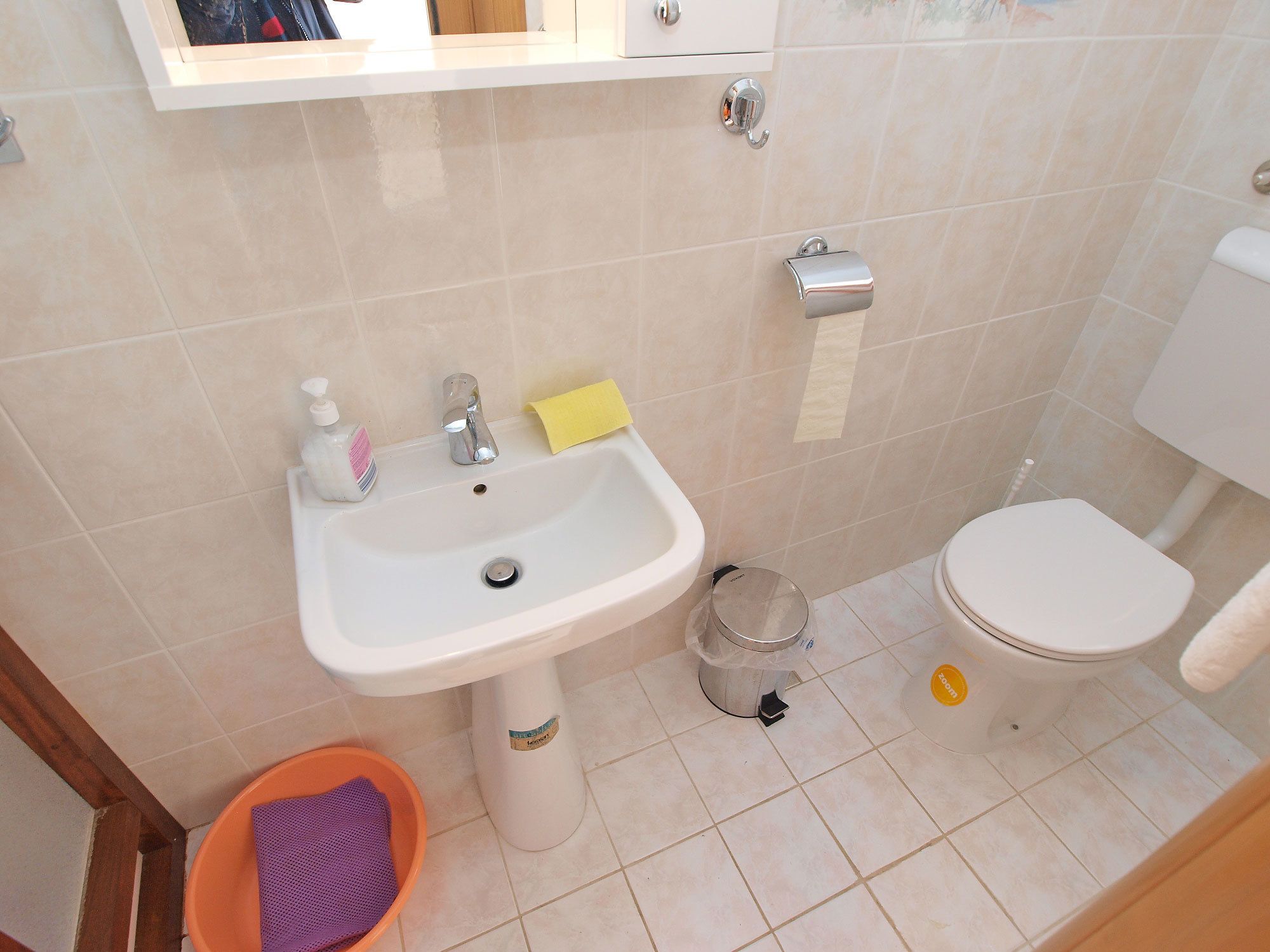 Et badeværelse med vask, toilet og en lille skraldespand.