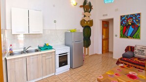 Una cocina compacta con refrigerador, horno y lavamanos. Hay una mesa de madera con mantel floral y un cuadro de colores en la pared.
