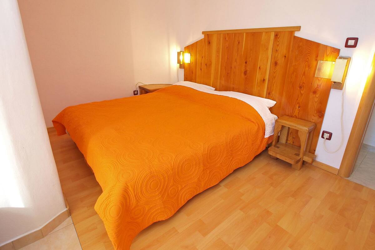 A single-bed room with a wooden headboard, two bedside lamps, and a small wooden bench.