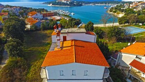 Un edificio costero con techo de tejas rojas, un balcón y vistas al mar y al puerto deportivo.
