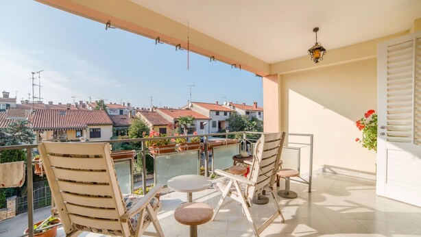 A balcony with two chairs and a table, overlooking a residential area with red-tiled roofs. - Apartment Lucio 804 (Porec)