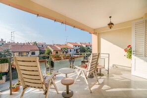 Een balkon met twee stoelen en een tafel, uitkijkend op een woongebied met rode dakpannen.