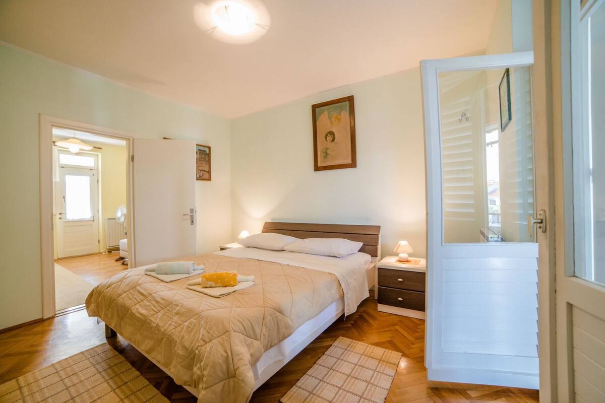 A bedroom with a bed, bedside tables, a nightstand, a door, and a window.