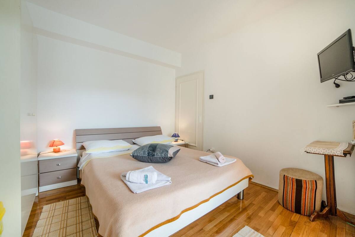A neatly arranged bedroom with a bed, bedside tables, a TV, and a small stool.