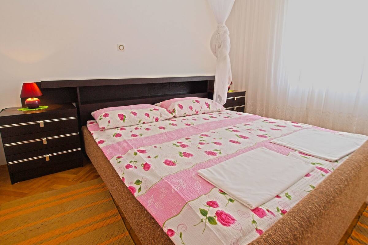 A neatly made bed with a floral bedspread, a bedside table with a lamp, and a nightstand with drawers.