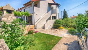 A two-story house with a stone staircase leading to the entrance, surrounded by a well-maintained garden with various plants and flowers. - Apartment Hasima 116 (Medulin)
