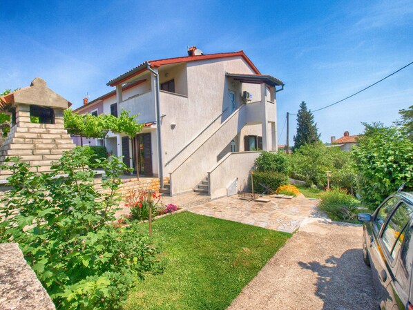 A two-story house with a stone staircase leading to the entrance, surrounded by a well-maintained garden with various plants and flowers.