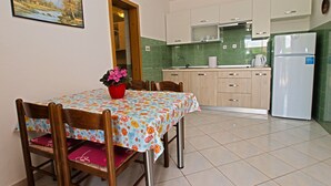 A dining area with a table set for four, a kitchen with green tiles, and a refrigerator. - Apartment Hasima 116 (Medulin)