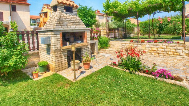 A stone-built outdoor kitchen with a chimney, surrounded by a well-maintained garden with various plants and flowers. - Apartment Hasima 116 (Medulin)