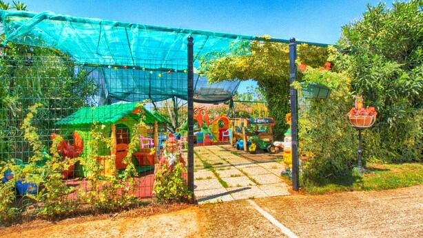 A garden with a play area, including a slide and climbing structures, enclosed by a wire fence. - Apartments Anka 1223 (Vodnjan)