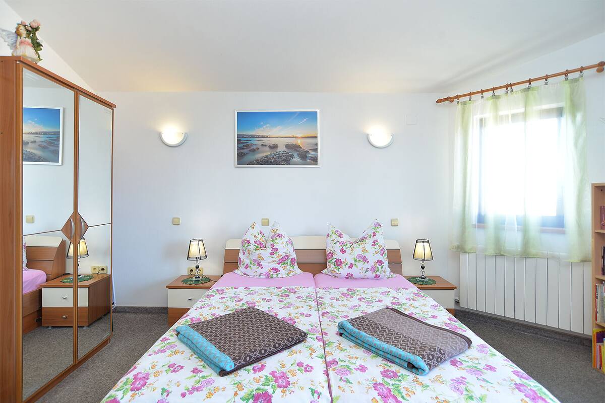 A bedroom with a bed, bedside tables, a mirror, a picture on the wall, and a window with curtains.