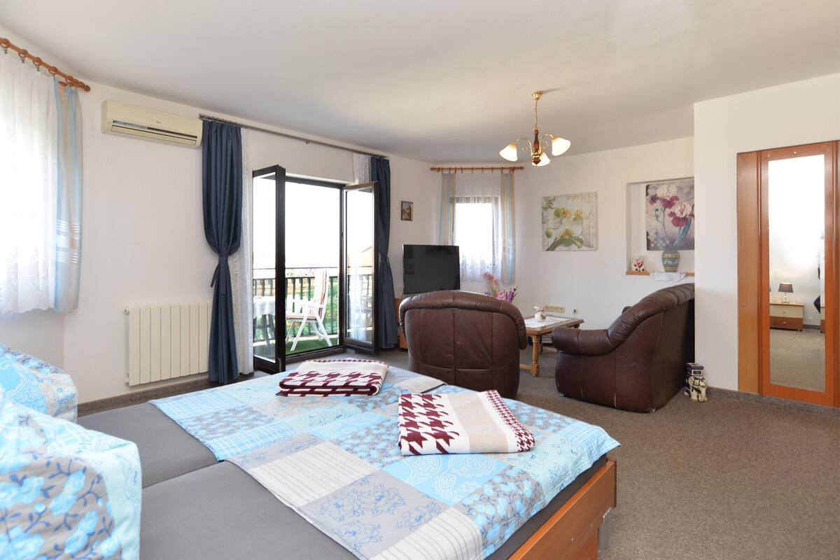 A bedroom with a bed, a chair, a small table, and a balcony with a view.