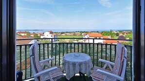 A balcony with two chairs and a table, overlooking a coastal town with houses and the sea. - Apartments Anka 1223 (Vodnjan)