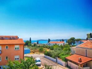 Ein Küstenwohngebiet mit Häusern mit Terrakotta-Dächern, bewölktem, blauem Himmel und Blick auf das Meer.
