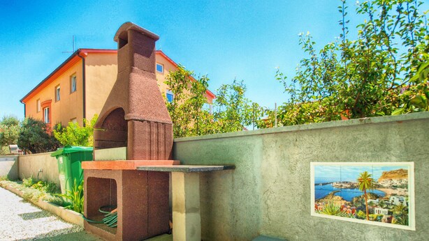 A house with a chimney, a green trash bin, and a wall-mounted picture. - Apartments Ankica 1420 (Fazana)