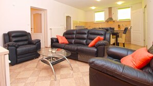 A living room with a glass coffee table, two black leather sofas with red cushions, and a kitchen in the background. - Apartments Ankica 1420 (Fazana)