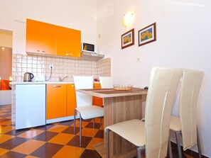 Cozinha compacta com armários laranjas, micro-ondas e um pequeno espaço de refeições com mesa de madeira e cadeiras brancas.