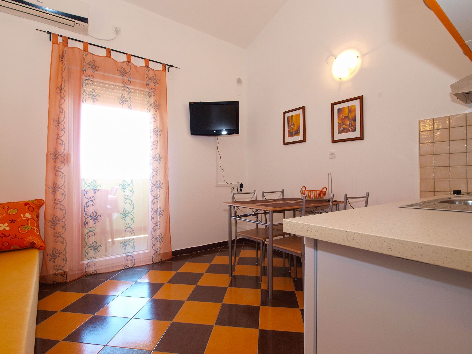 Une cuisine de taille réduite avec un coin repas, un téléviseur fixé au mur et un carrelage à motifs à carreaux.