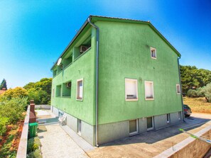 Ein zweistöckiges Haus mit grüner Fassade, mehreren Fenstern und einem kleinen Balkon.