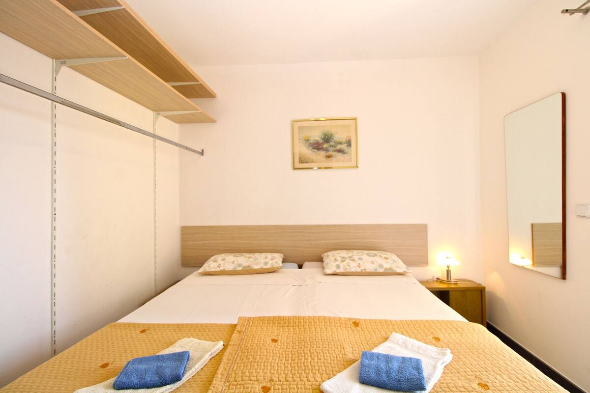 A hotel room with a bed, two pillows, a bedside lamp, a framed picture on the wall, and a mirror.