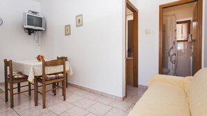 Une petite pièce, bien rangée, avec une table à manger, un canapé et un téléviseur fixé au mur.