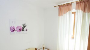 Une chambre à coucher comprenant un lit, une table de chevet, un tableau décoratif au mur et une fenêtre avec des rideaux.