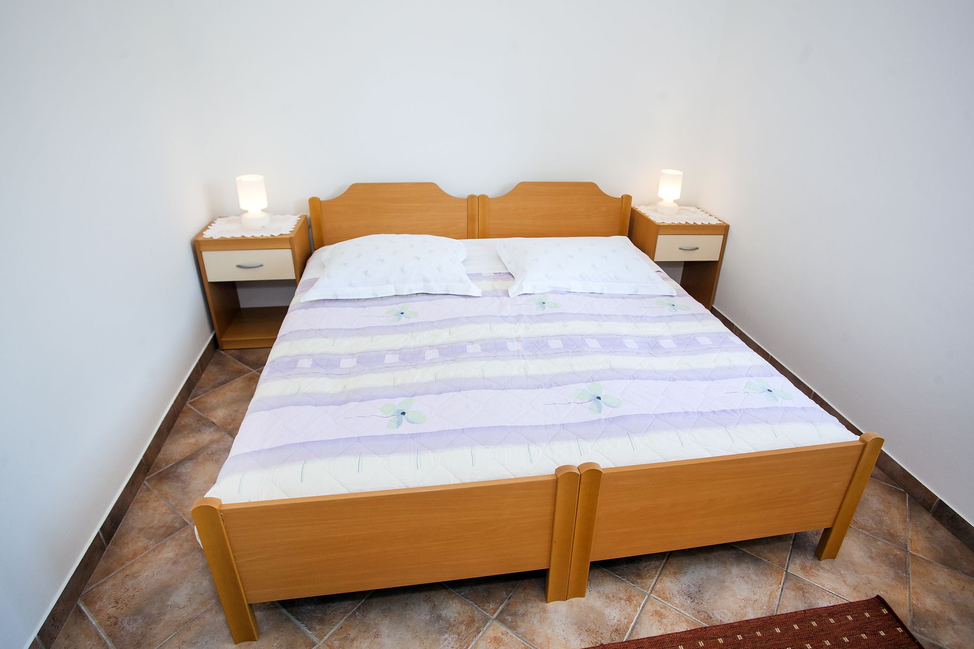 Una cama individual con estructura de madera, dos mesitas de noche con lámparas y una colcha estampada.