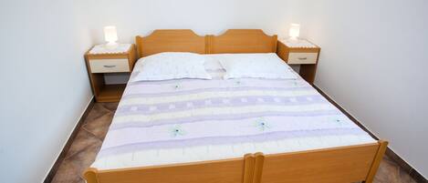 Una cama individual con estructura de madera, dos mesitas de noche con lámparas y una colcha estampada.