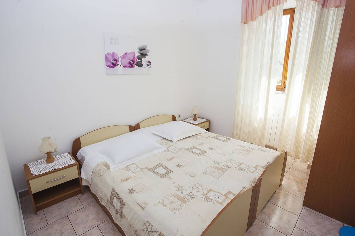 Quarto com cama, mesa de cabeceira, abajur e um objeto decorativo na parede.