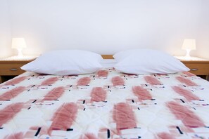 A bed with a patterned bedspread, two white pillows, and two bedside lamps on wooden nightstands. - Apartments Antonieta 1209 (Medulin)