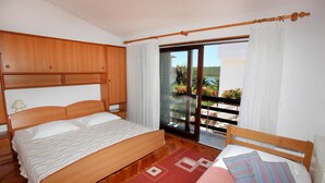 A bedroom with a wooden bed, a nightstand, a window with curtains, and a view of the outdoors. - Apartements Antonia 1208 (Medulin)
