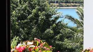 A view from a balcony with lush greenery and a body of water in the background. - Apartements Antonia 1208 (Medulin)