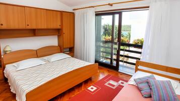 A bedroom with a wooden bed, a nightstand, a wardrobe, and a balcony with a view of greenery.