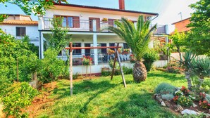 A two-story house with a balcony, surrounded by a garden with various plants and a palm tree. - Apartements Antonia 1208 (Medulin)