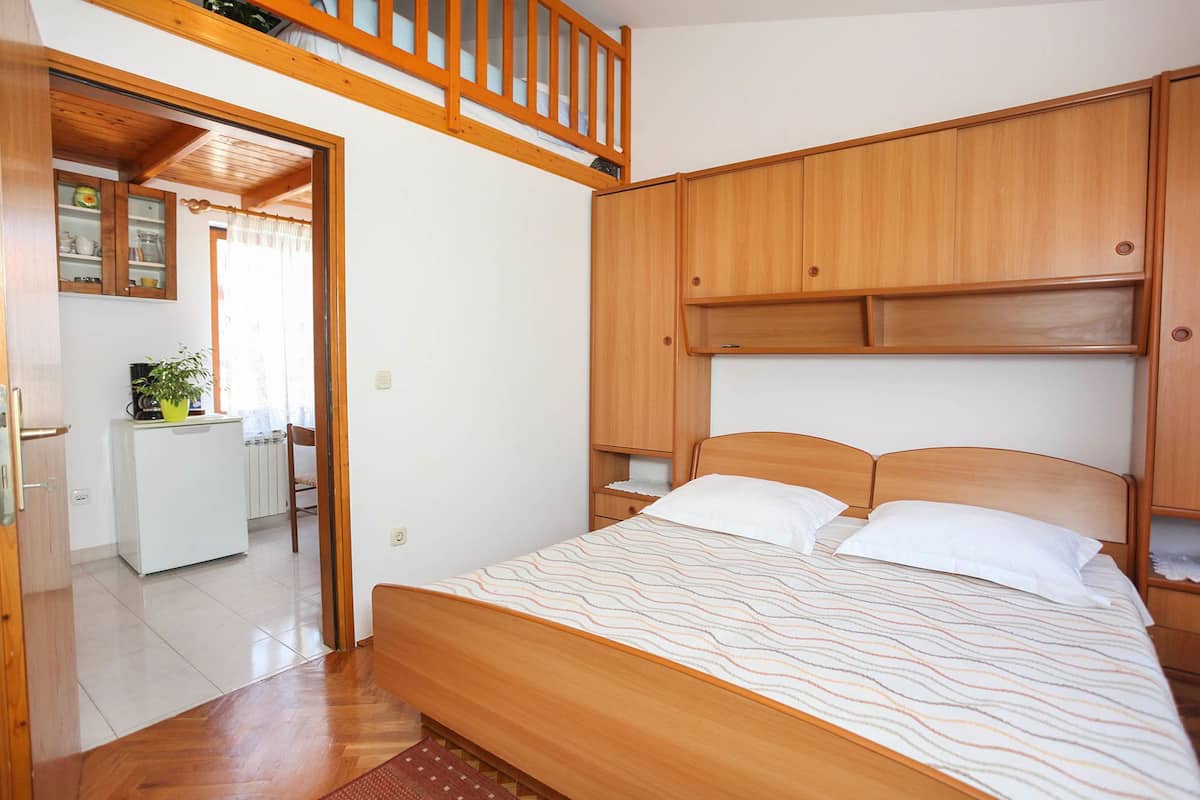 A bedroom with a wooden bed, a built-in wardrobe, and a kitchenette area.
