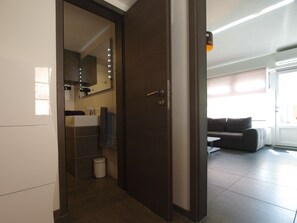 Un baño moderno con una puerta de madera oscura, un espejo con iluminación, un lavamanos blanco y una toalla colgada en la pared.