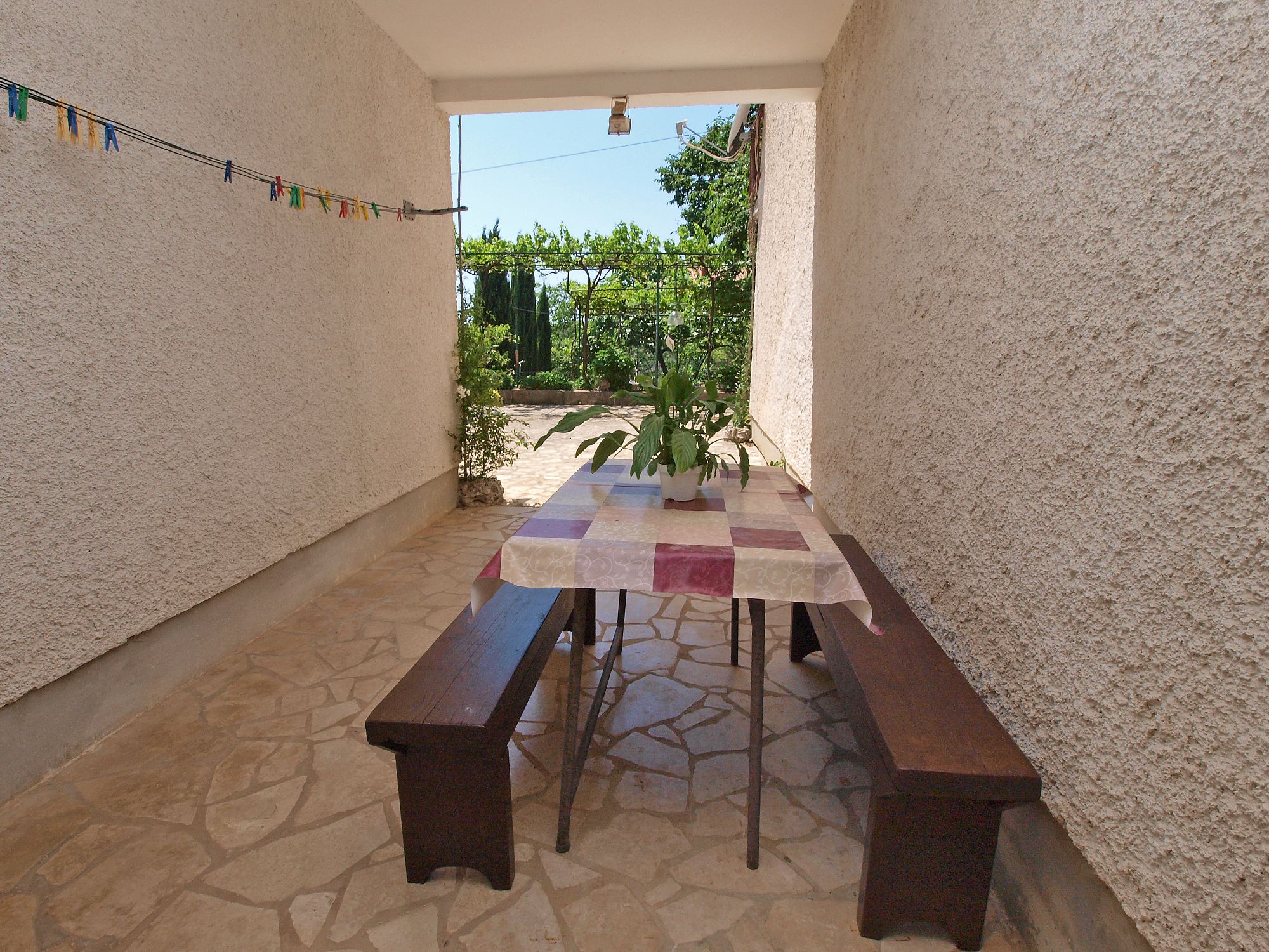 A covered outdoor patio with a checkered table and benches, surrounded by textured walls and a stone floor.