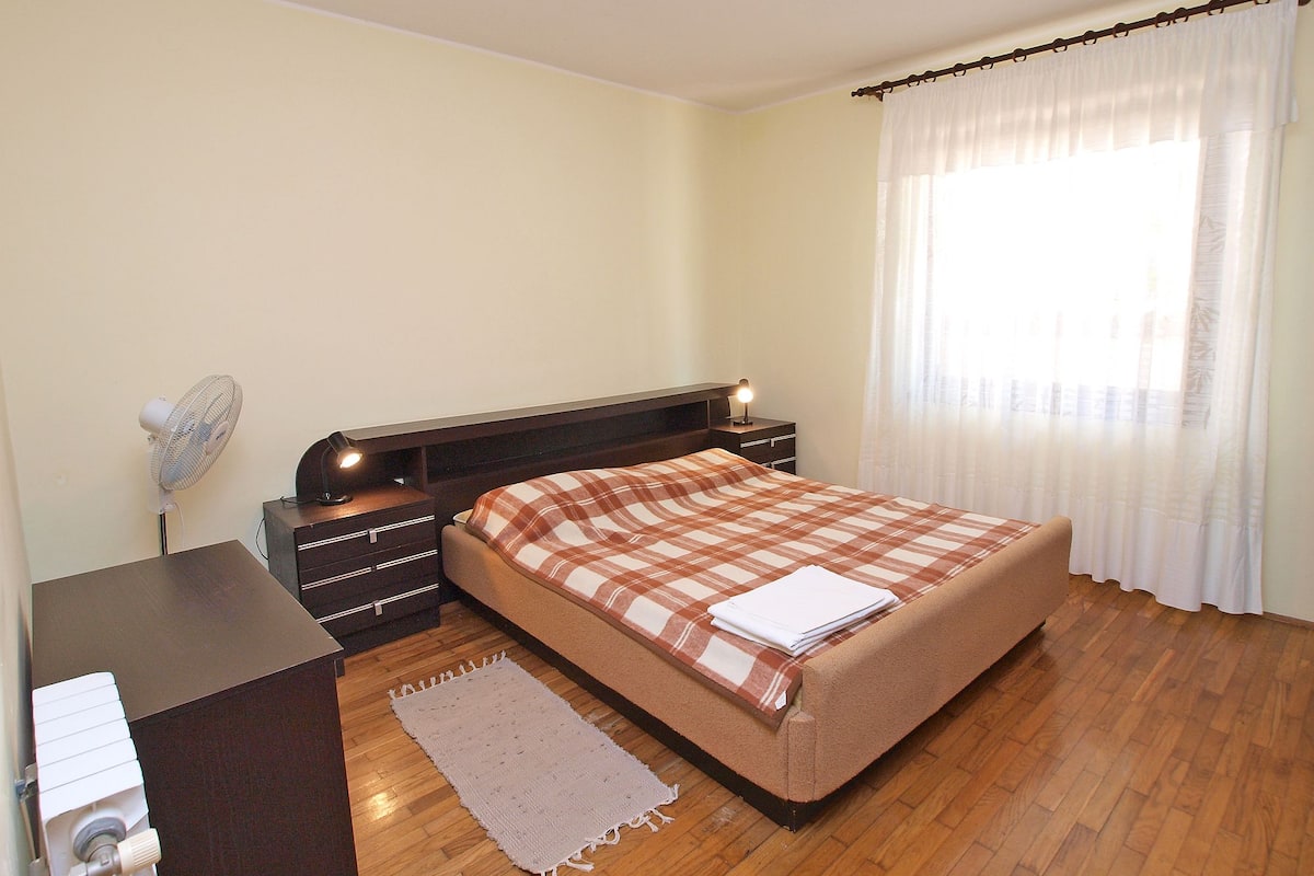Une chambre à coucher avec un lit, une table de chevet, une lampe et une fenêtre avec des rideaux.