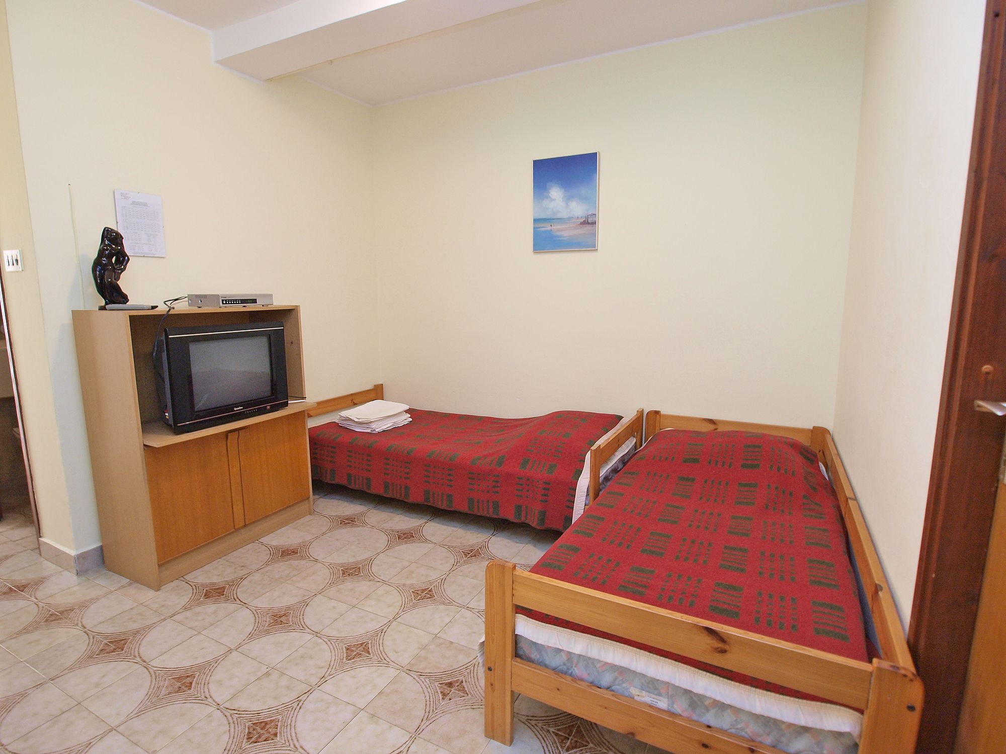 Een kleine kamer met een bed, een televisie op een houten standaard en een vloer met een patroon.